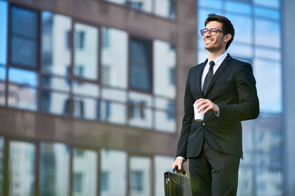 Cheerful banker in formalwear having coffee on his way to work in the morning - Photo, Image
