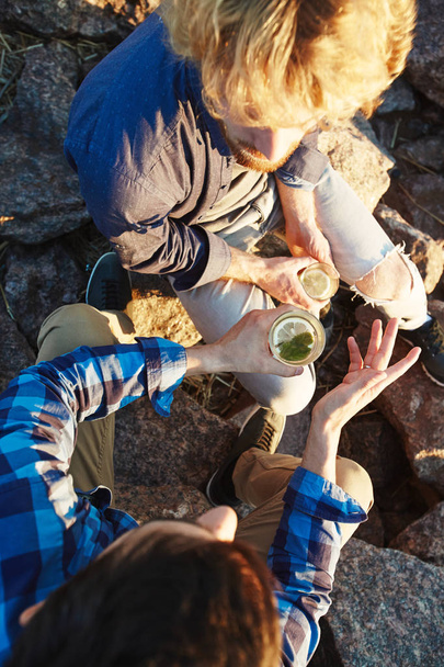 Katsaus kahteen nuoreen mieheen juomassa istuessaan kivillä ulkona
 - Valokuva, kuva