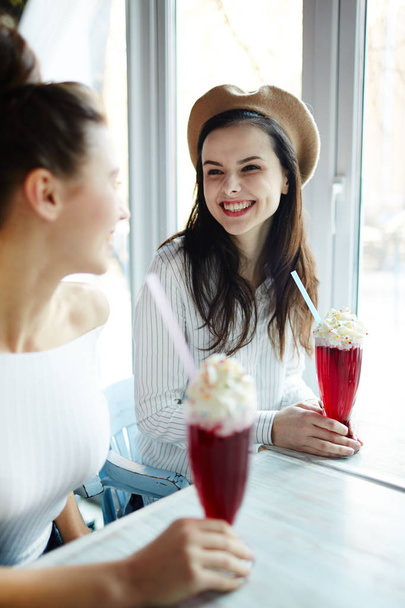 Onnellinen tyttö hammas hymy katselee hänen ystävänsä aikana puhua cocktail kahvilassa
 - Valokuva, kuva