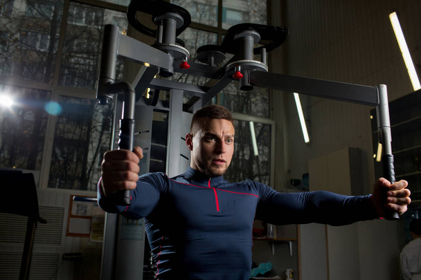 Сильный молодой спортсмен делает упражнения для мышц рук и бицепсов на спортивном оборудовании
 - Фото, изображение