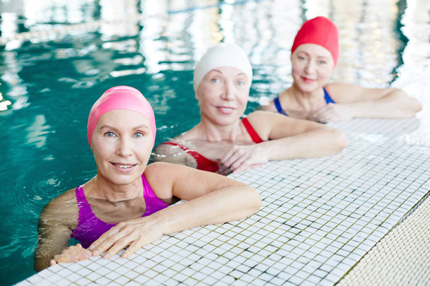 Grupa dojrzałych kobiet w strojach kąpielowych, siedząc w basenie i patrzy na Ciebie - Zdjęcie, obraz