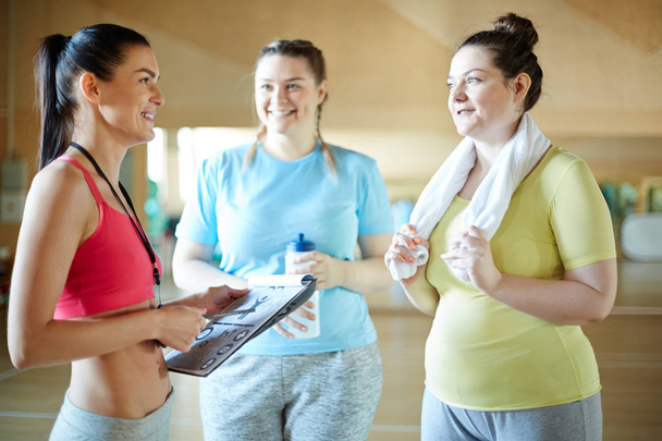Jovem mulher de tamanho superior com toalha conversando com instrutor de fitness após o treinamento
 - Foto, Imagem