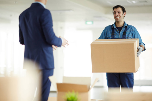 Jeune coursier transportant une grosse boîte à un employé de bureau tout en l'aidant à déménager
 - Photo, image