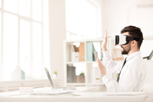Businessman using VR glasses sitting at table in office taking break from work - Photo, Image