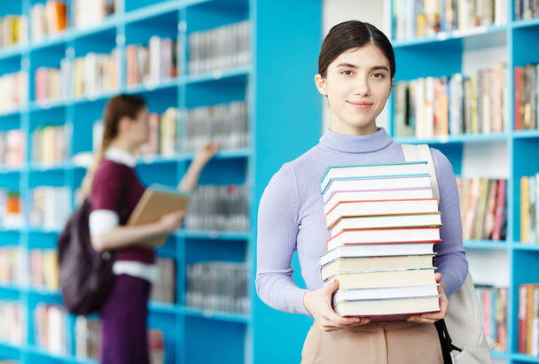 Erfolgreicher Student mit einem Stapel Bücher und Handbücher, der sie in die Universitätsbibliothek bringt - Foto, Bild