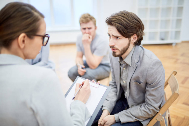 Troubled young businessman explaining his problem to counselor during group session - Photo, image