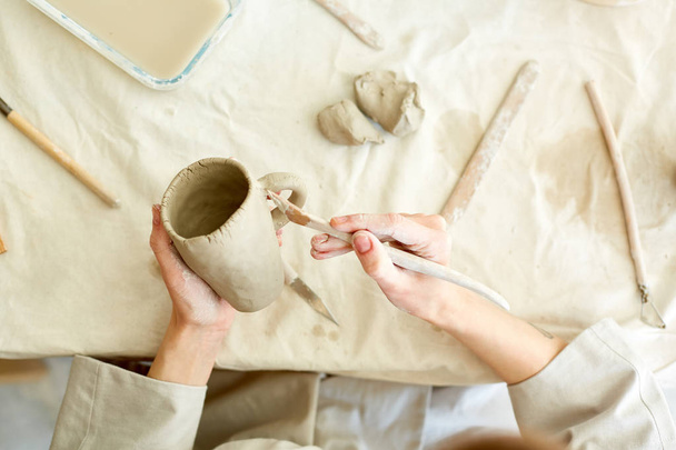 Робоча майстер обробки глиняного кухоль ручної роботи зі спеціальним рушником над столом
 - Фото, зображення