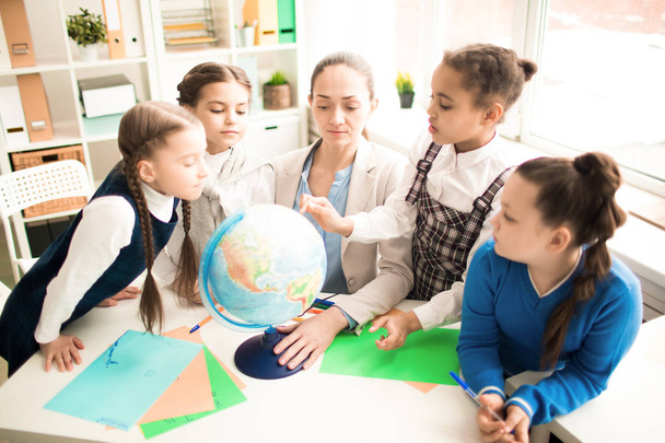 Söpö oppilaat ja opettaja luokkahuoneessa maapallon kanssa peruskoulussa
 - Valokuva, kuva