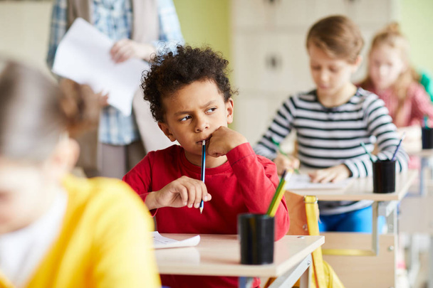 Pensive koulupoika istuu yksittäisten työpöytä ja ajatellut oikea vastaus kirjoittaessaan tentti testi
 - Valokuva, kuva