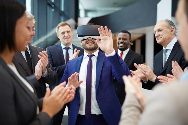 Young contemporary man in suit with vr goggles on his face taking part in virtual conference among applauding colleagues - Photo, image