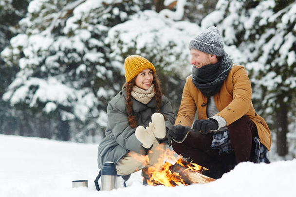 Két fiatal hátizsákos guggolva a hófúvás, és beszél, miközben felmelegedés a kezüket, tűzön - Fotó, kép