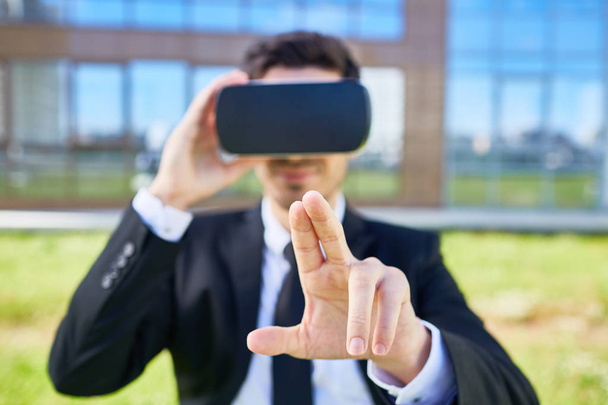 Молодий бізнесмен з окулярами vr, намагаючись натиснути уявну кнопку на віртуальному дисплеї на відкритому повітрі
 - Фото, зображення