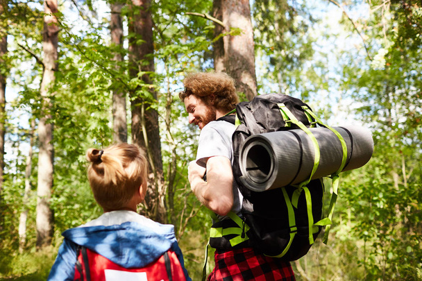 Father and son scouts with backpacks walking in the forest to their camp on sunny day - Photo, Image