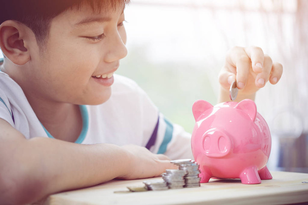 Ασιατικές αγόρι εξοικονόμηση χρημάτων σε ροζ κουμπαράς με πρόσωπο χαμόγελο . - Φωτογραφία, εικόνα