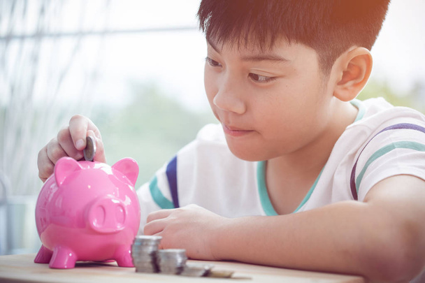 Ασιατικές αγόρι εξοικονόμηση χρημάτων σε ροζ κουμπαράς με πρόσωπο χαμόγελο . - Φωτογραφία, εικόνα