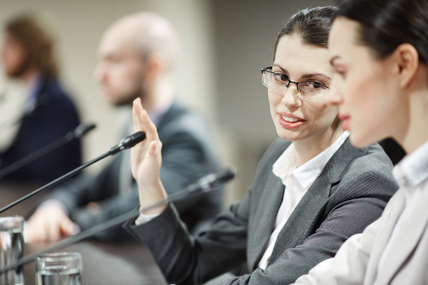 eine der Geschäftsfrauen, die das Mikrofon mit der Hand bedeckt, während sie sich mit ihrem Kollegen oder Delegierten berät - Foto, Bild