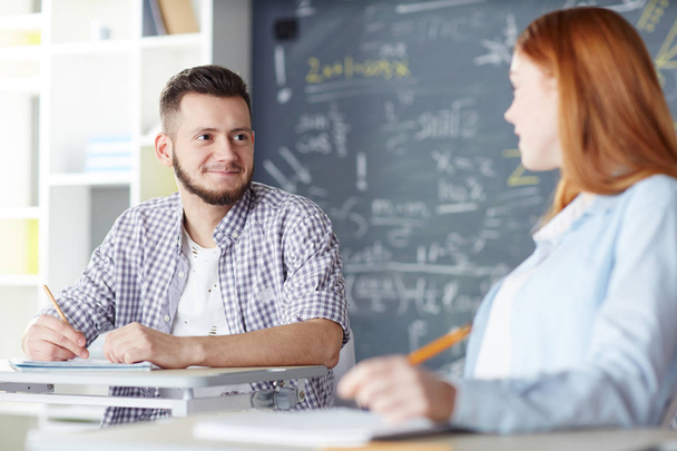 Happy guy and his girlfriend discussing homework points before lesson in classroom - Foto, Imagem