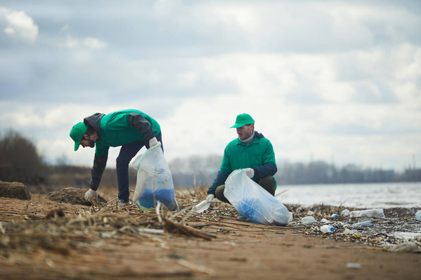 Mitarbeiter der Umweltorganisation sammeln Müll aus schmutzigem Gebiet und verwerten ihn in spezielle Säcke - Foto, Bild