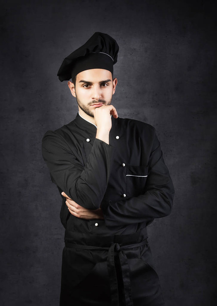 Portrait of a thinking chef cooker in black uniform, gray background - Photo, image