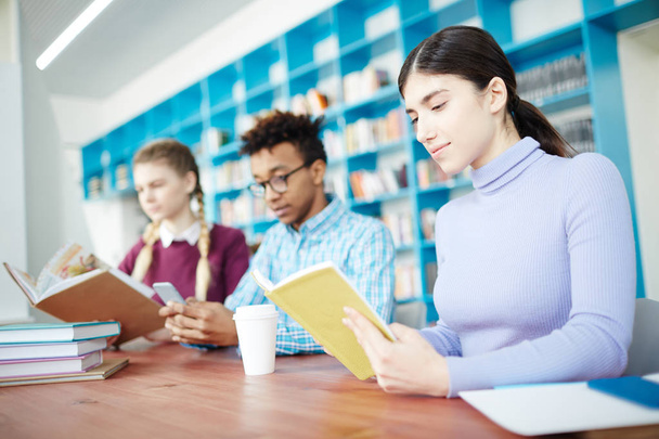 umtriebige junge Studenten mit Büchern, die in Reihe am Schreibtisch sitzen und nach dem Unterricht in der Bibliothek lesen - Foto, Bild