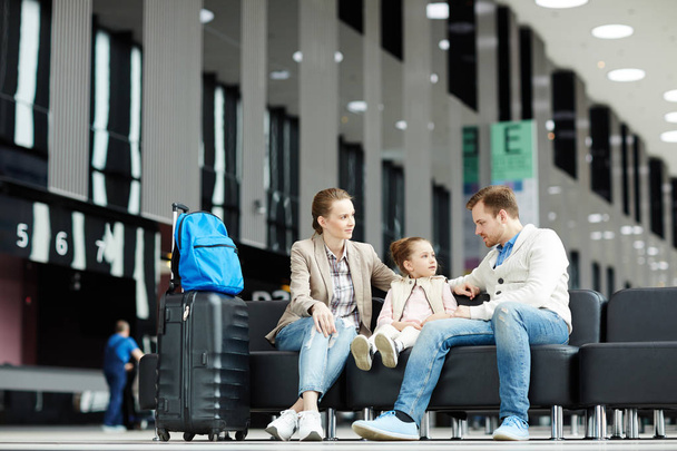 Cute little girl sitting on leather sofa between her parents while waiting for departure announcement - Photo, Image