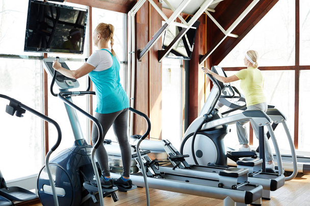 Deux femmes mûres sportives en vêtements de sport faisant de l'exercice sur leur équipement d'entraînement dans une salle de gym moderne
 - Photo, image