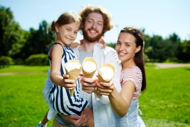 Jovens pais felizes e sua filha mostrando gelados de cone enquanto passam o dia de verão no parque
 - Foto, Imagem