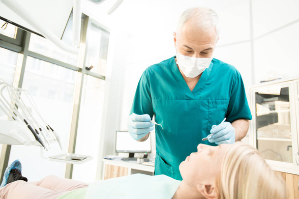 Check-up önce onun hasta üzerinde aletleri ile eğilerek üniformalı profesyonel diş hekimi - Fotoğraf, Görsel