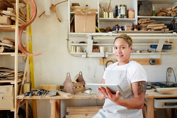 Молодая женщина в рабочей одежде ищет сайты о столярных изделиях и деревянных предметах
 - Фото, изображение