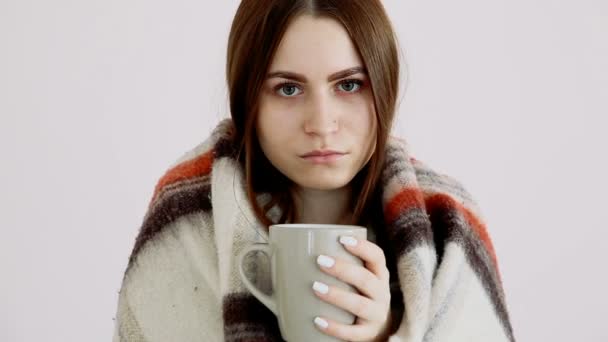 una hermosa chica fría de apariencia eurareana en una manta de lana está bebiendo té caliente en la pared blanca
. - Imágenes, Vídeo