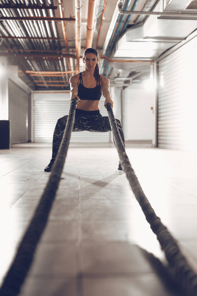 Молода м'язиста жінка займається з мотузками в гаражному тренажерному залі
 - Фото, зображення
