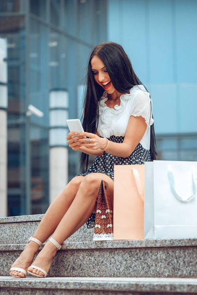 Молода жінка з сумками для покупок за допомогою смартфона після покупки
 - Фото, зображення