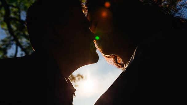 tender touches of the lips of a young couple against the background of bright sunlight on a wonderful summer day - Фото, зображення