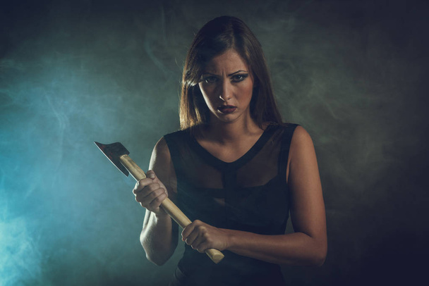 mujer peligrosa con hacha oxidada en habitación oscura ahumada
 - Foto, Imagen