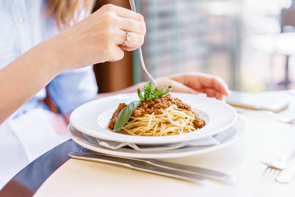 Young happy woman sitting at the table in cafe and enjoying the meal. Hungry woman eating tasty pasta. Dish of spaghetti Bolognese - Photo, Image