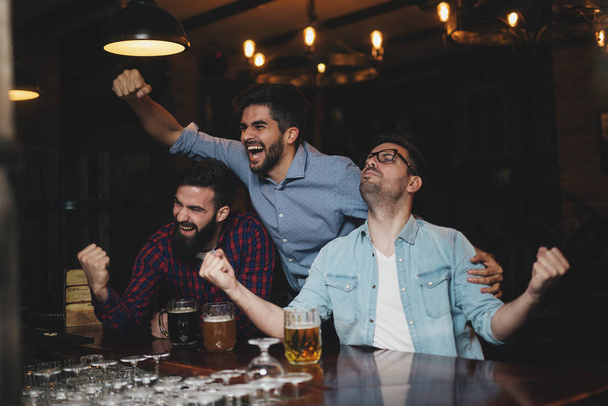 die Jungs in der Kneipe trinken Bier und schauen sich das Fußballspiel an - Foto, Bild
