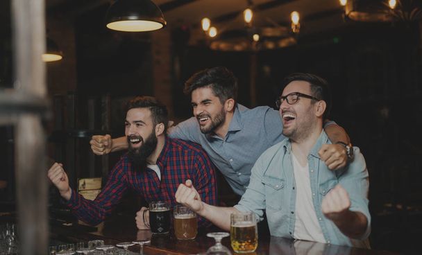 Парни в пабе пьют пиво и смотрят футбольный матч
 - Фото, изображение