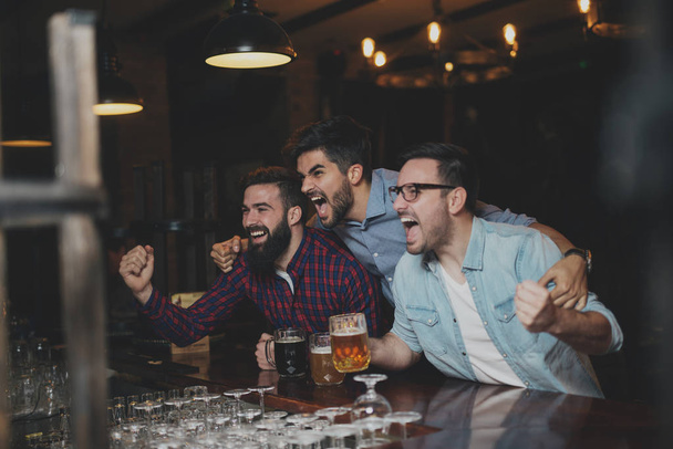 Хлопці в пабі п'ють пиво і дивиться футбольний матч
 - Фото, зображення