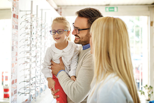 Familia feliz eligiendo gafas en la tienda de óptica
.  - Foto, imagen