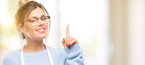Majitel obchodu mladá žena nosí zástěru šťastný a překvapení jásající exprimují wow gesto směřující nahoru - Fotografie, Obrázek