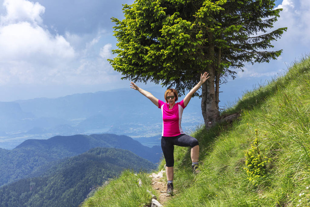 Active woman hiking in the mountains above the valley. Narrow trail on the steep slope. Trekking in the national park with beautiful scenery around. - Photo, Image