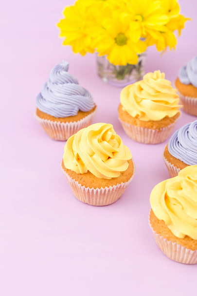 Cupcakes decorados con crema amarilla y violeta y crisantemos sobre fondo pastel violeta. Área de copyspace. Se puede utilizar para el saludo, los días de la madre y la tarjeta de San Valentín. Concepto de minimalismo
. - Foto, imagen