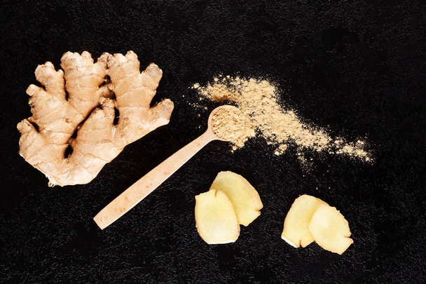 Fresh and ground ginger root on wooden spoon on black background. Natural remedy. - Foto, Bild