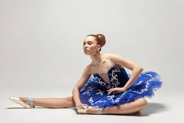 attractive ballerina in blue dress graceful sitting on white studio floor  - Foto, imagen