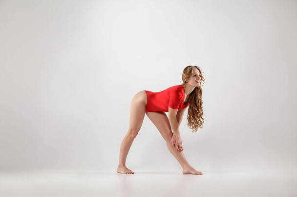 attractive athletic woman in red leotard doing yoga pose isolated on white studio background  - 写真・画像