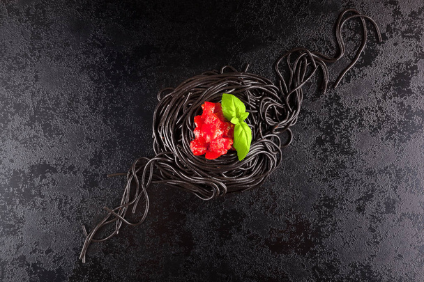 Tintahal fekete spagetti bazsalikomos paradicsom fölött sötét felületre. - Fotó, kép