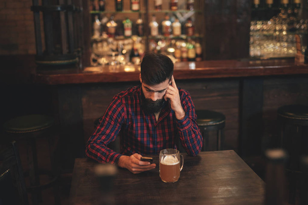 Молодой красивый мужчина с пивом с мобильного в пабе
 - Фото, изображение