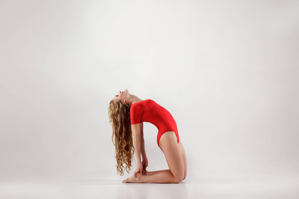 woman with long hair in red leotard balancing on hands and knees while doing camel yoga pose  - Photo, image