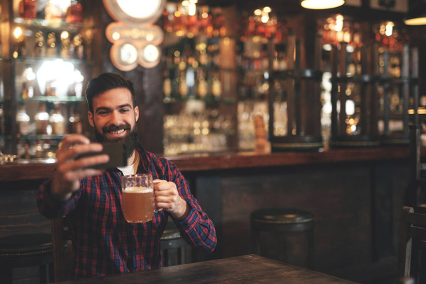 Молодой бородатый мужчина с пивом веселится в пабе
 - Фото, изображение