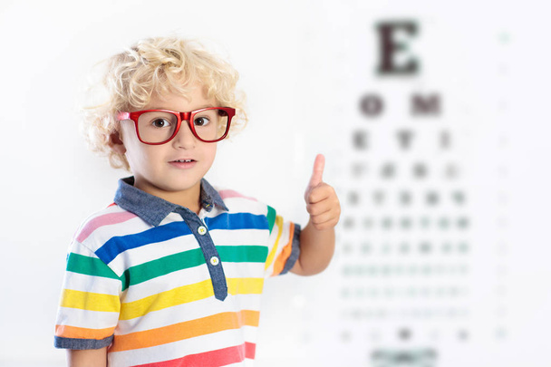 Lapsi tähtäimessä. Lapsi valitsee silmälasit optiikkakaupasta. Näönmittaus koululaisille. Silmien kulumista lapsille. Lääkäri tekee silmätarkastuksen. Silmälasipäinen poika kirjainkaaviossa. - Valokuva, kuva